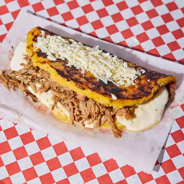 Venezuelan cachapa from La Latina, filled with shredded beef, white cheese, and cream on checkered paper.