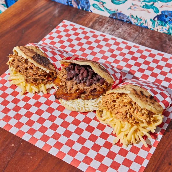 Three Venezuelan arepas, one with shredded beef and cheese, one with black beans and plantains, and one with shredded chicken.