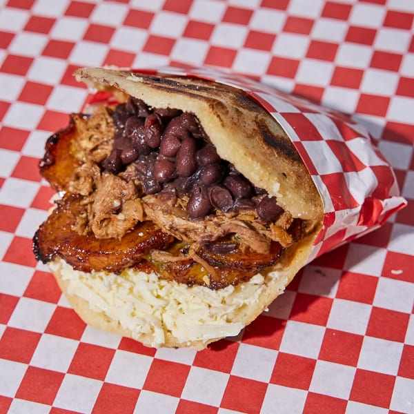 La Latina's Venezuelan arepa filled with black beans, shredded meat, plantains, and cheese, on checkered paper.