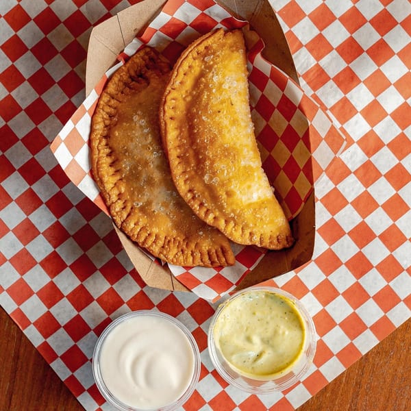 Two golden-brown Venezuelan empanadas in a paper tray with red and white checkered lining, with two dipping sauces.
