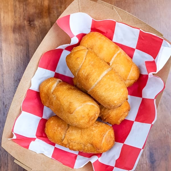 Golden-brown Venezuelan tequeños, cheese-filled fried bread sticks, in a paper tray with red and white checkered lining.